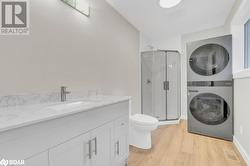 Bathroom featuring toilet, hardwood / wood-style flooring, vanity, walk in shower, and stacked washer / drying machine - 