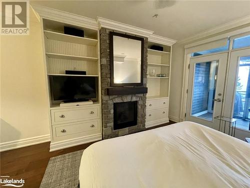 Bedroom featuring dark wood-type flooring, a stone fireplace, french doors, and crown molding - 1869 Muskoka Road 118 W Unit# L204-D2, Muskoka Lakes, ON - Indoor Photo Showing Bedroom