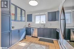 Kitchen with light tile patterned flooring, blue cabinetry, appliances with stainless steel finishes, decorative backsplash, and sink - 