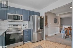 Kitchen featuring blue cabinetry, decorative backsplash, stainless steel appliances, and light tile patterned flooring - 