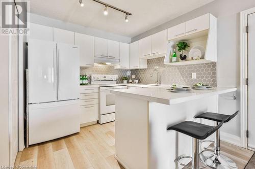 Kitchen featuring backsplash, white cabinetry, light wood-type flooring, a kitchen bar, and white appliances - 2030 Cleaver Avenue Unit# 122, Burlington, ON - Indoor Photo Showing Kitchen