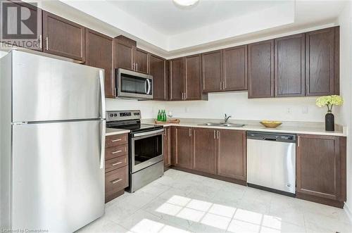 Kitchen featuring dark brown cabinetry, light tile patterned flooring, sink, appliances with stainless steel finishes, and a tray ceiling - 88 Decorso Drive Unit# 44, Guelph, ON - Indoor Photo Showing Kitchen With Double Sink