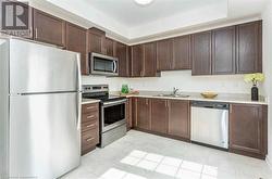 Kitchen featuring dark brown cabinetry, light tile patterned flooring, sink, appliances with stainless steel finishes, and a tray ceiling - 