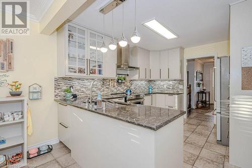 Kitchen with hanging light fixtures, wall chimney range hood, dark stone counters, and kitchen peninsula - 2378 Headon Road, Burlington, ON - Indoor Photo Showing Kitchen With Upgraded Kitchen