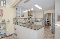 Kitchen with hanging light fixtures, wall chimney range hood, dark stone counters, and kitchen peninsula - 