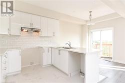 Kitchen featuring pendant lighting, kitchen peninsula, sink, backsplash, and white cabinetry - 