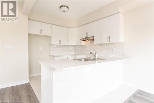 Kitchen featuring white cabinetry, light wood-type flooring, decorative backsplash, sink, and kitchen peninsula - 620 Colborne Street W Unit# 42, Brantford, ON - Indoor Photo Showing Kitchen