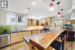 Kitchen with sink, custom range hood, light brown cabinets, light wood-type flooring, and appliances with stainless steel finishes - 