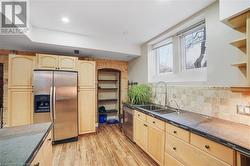 Kitchen with stainless steel appliances, light wood-type flooring, light brown cabinetry, decorative backsplash, and sink - 