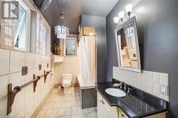 Bathroom with toilet, an inviting chandelier, tile walls, tile patterned flooring, and vanity - 