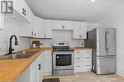 Kitchen featuring butcher block countertops, tasteful backsplash, white cabinets, and stainless steel appliances - 