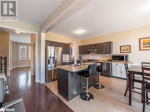 Kitchen with a center island with sink, stainless steel appliances, dark brown cabinetry, a kitchen bar, and light hardwood / wood-style floors - 3046 Stone Ridge Boulevard, Orillia, ON - Indoor Photo Showing Kitchen With Stainless Steel Kitchen