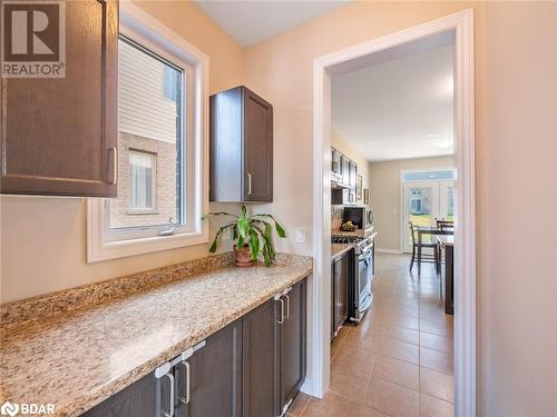 Kitchen featuring light stone counters, dark brown cabinets, appliances with stainless steel finishes, and light tile patterned floors - 3046 Stone Ridge Boulevard, Orillia, ON - Indoor