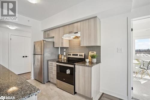 Kitchen featuring appliances with stainless steel finishes, light brown cabinetry, decorative backsplash, dark stone countertops, and light hardwood / wood-style flooring - 8 Culinary Lane Unit# 402, Barrie, ON - Indoor Photo Showing Kitchen