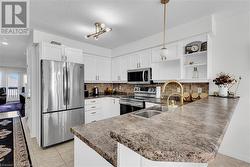 Kitchen featuring appliances with stainless steel finishes, pendant lighting, sink, white cabinets, and kitchen peninsula - 