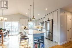 Kitchen with white cabinetry, vaulted ceiling, light hardwood / wood-style floors, and stainless steel appliances - 