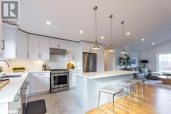 Kitchen featuring white cabinetry, sink, appliances with stainless steel finishes, a kitchen island, and pendant lighting - 