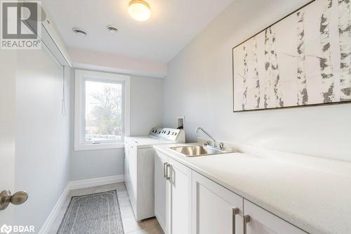 Laundry room with light tile patterned flooring, cabinets, sink, and washer and dryer - 1647 Lakeside Drive, Hillier, ON - Indoor Photo Showing Laundry Room