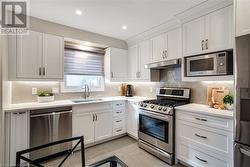 Kitchen with stainless steel appliances, light quartz counters, white cabinets, backsplash - 