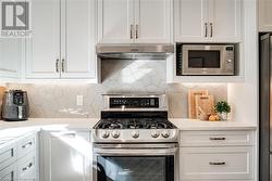 Kitchen with stainless steel appliances, light quartz counters, white cabinets, backsplash - 