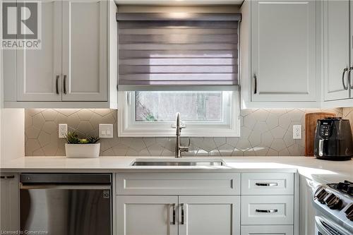 Kitchen with stainless steel appliances, light quartz counters, white cabinets, backsplash. Custom window covering - 2301 Cavendish Drive Unit# 106, Burlington, ON - Indoor Photo Showing Kitchen