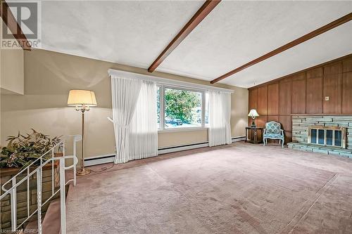 Living room with vaulted, beamed ceiling, a stone fireplace, mahogany paneling, and carpeted floors - 16 Harvest Lane, Brantford, ON - Indoor With Fireplace