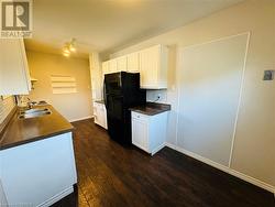 Kitchen featuring white cabinetry, black fridge, sink, dark wood-type flooring, and decorative backsplash - 