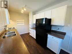 Kitchen featuring tasteful backsplash, black fridge, white cabinetry, dark hardwood / wood-style floors, and sink - 