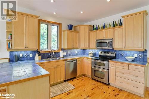 Kitchen featuring tile countertops, sink, appliances with stainless steel finishes, light brown cabinetry, and light hardwood / wood-style flooring - 1320 360 Island, Port Severn, ON - Indoor Photo Showing Kitchen With Double Sink