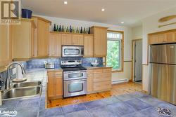 Kitchen with stainless steel appliances, light brown cabinets, sink, hardwood / wood-style flooring, and tile counters - 