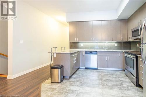 Kitchen featuring sink, kitchen peninsula, appliances with stainless steel finishes, light stone countertops, and light wood-type flooring - 62 Balsam Street Unit# T113, Waterloo, ON - Indoor Photo Showing Kitchen