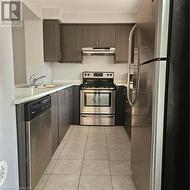 Kitchen featuring range hood, stainless steel range oven, refrigerator, dishwashing machine, and light tile patterned floors - 