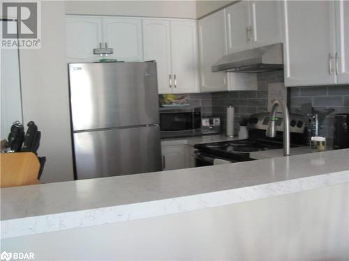 Kitchen featuring white cabinets, range hood, tasteful backsplash, and stainless steel appliances - 150 E Dunlop Street E Unit# 605, Barrie, ON 