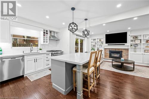 Kitchen with stainless steel appliances, white cabinetry, wall chimney exhaust hood, decorative light fixtures, and a kitchen island - 2401 Coventry Way, Burlington, ON 