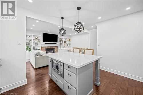 Kitchen with a fireplace, a kitchen island, dark hardwood / wood-style floors, pendant lighting, and stainless steel microwave - 2401 Coventry Way, Burlington, ON 