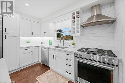 Kitchen featuring white cabinets, wall chimney range hood, sink, and appliances with stainless steel finishes - 2401 Coventry Way, Burlington, ON 