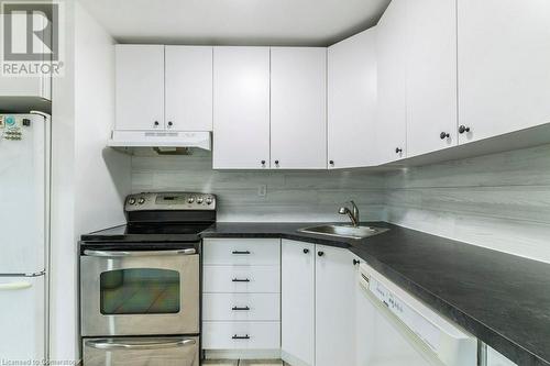 Kitchen featuring white cabinets, sink, white appliances, and backsplash - 48 Windom Road Unit# E, Kitchener, ON 