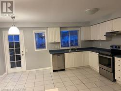 Kitchen with white cabinetry, appliances with stainless steel finishes, light tile patterned floors, hanging light fixtures, and sink - 