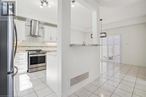 Kitchen with white cabinetry, appliances with stainless steel finishes, wall chimney exhaust hood, backsplash, and hanging light fixtures - 21 White Star Lane, Grimsby, ON 