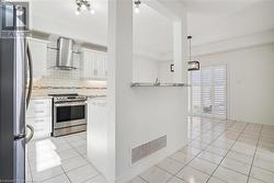 Kitchen with white cabinetry, appliances with stainless steel finishes, wall chimney exhaust hood, backsplash, and hanging light fixtures - 