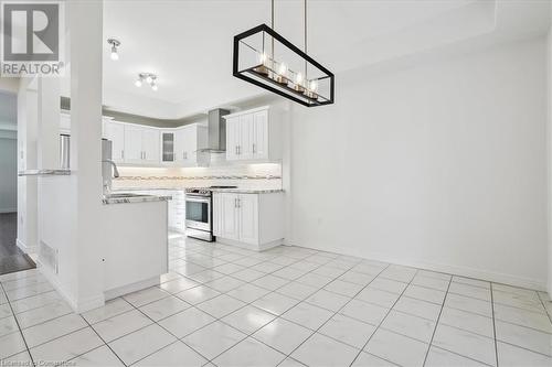 Kitchen with light tile patterned flooring, sink, stainless steel electric range, white cabinets, and wall chimney range hood - 21 White Star Lane, Grimsby, ON 