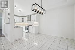 Kitchen with light tile patterned flooring, sink, stainless steel electric range, white cabinets, and wall chimney range hood - 