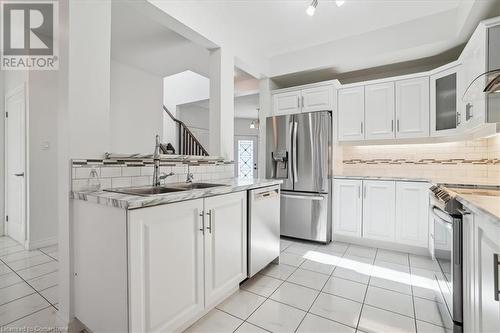 Kitchen with sink, appliances with stainless steel finishes, light tile patterned floors, backsplash, and white cabinets - 21 White Star Lane, Grimsby, ON 