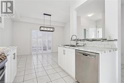 Kitchen featuring stainless steel appliances, white cabinetry, pendant lighting, light stone countertops, and sink - 