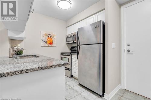 Kitchen with stainless steel appliances, light tile patterned floors, sink, light stone countertops, and white cabinetry - 2379 Central Park Drive Unit# 206, Oakville, ON - Indoor Photo Showing Kitchen