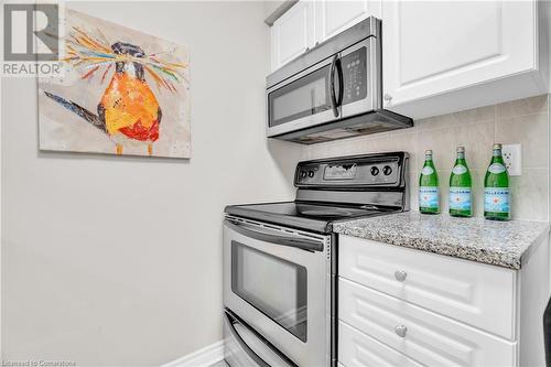 Kitchen with white cabinetry, appliances with stainless steel finishes, decorative backsplash, and light stone countertops - 2379 Central Park Drive Unit# 206, Oakville, ON - Indoor Photo Showing Kitchen