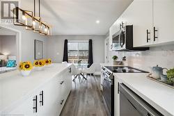 Kitchen featuring stainless steel appliances, hardwood / wood-style floors, tasteful backsplash, white cabinetry, and decorative light fixtures - 