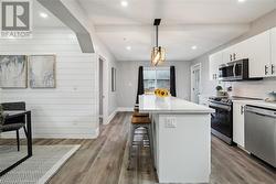 Kitchen with appliances with stainless steel finishes, light hardwood / wood-style flooring, pendant lighting, white cabinets, and a center island - 