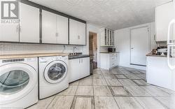 Laundry area with light tile patterned floors, cabinets, sink, and washing machine and clothes dryer - 