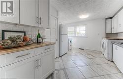 Kitchen with butcher block counters, white appliances, white cabinetry, and backsplash - 